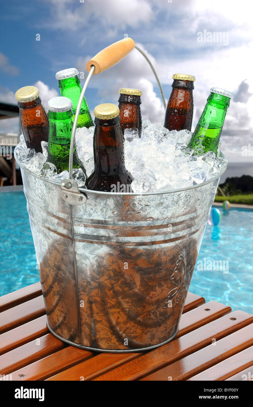 Close up of a beer bucket on poolside teak table. Swimming pool with beach  balls and house in background Stock Photo - Alamy