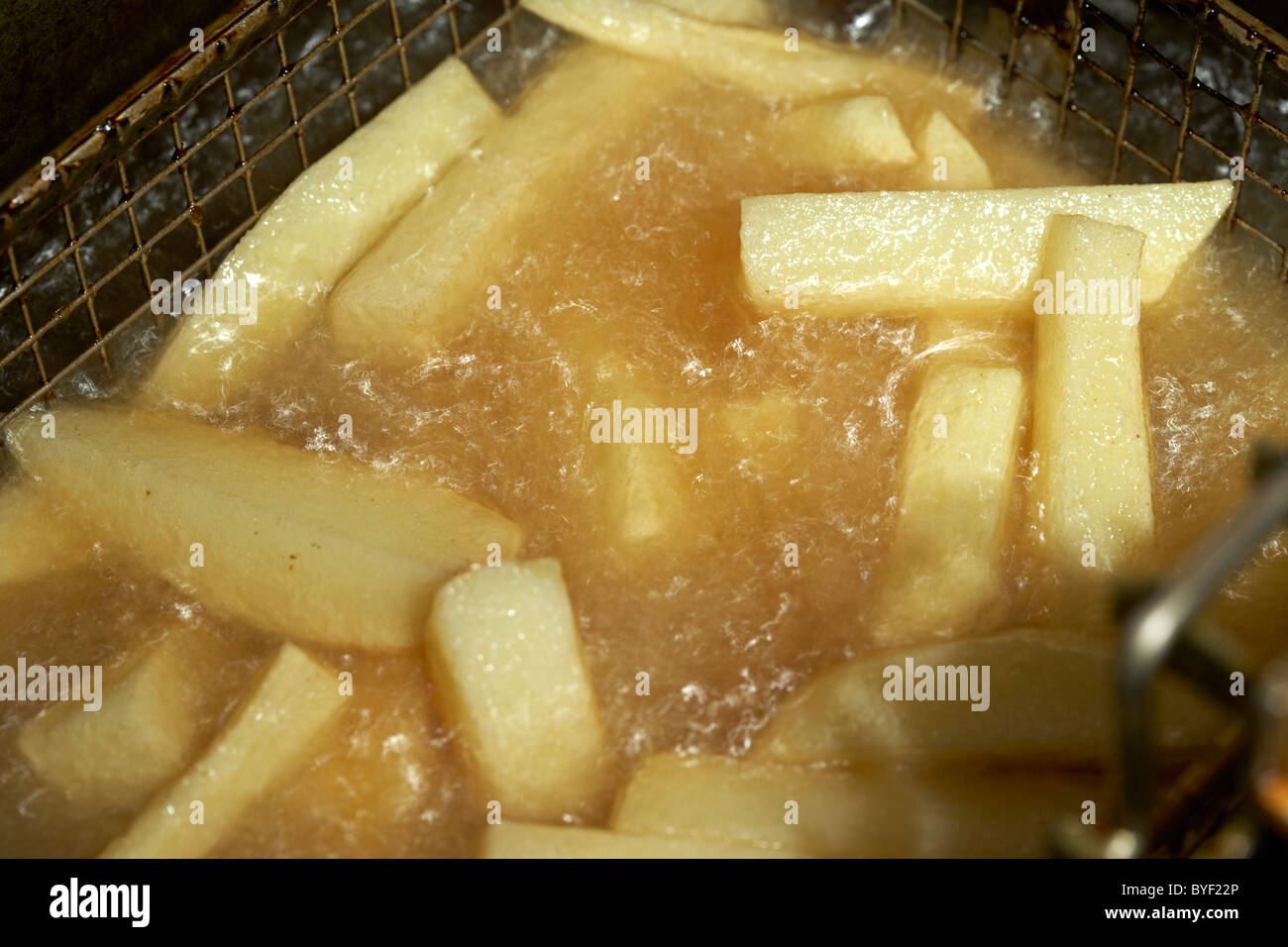 frying freshly cut home made chips from irish potatoes in a deep fat fryer Stock Photo