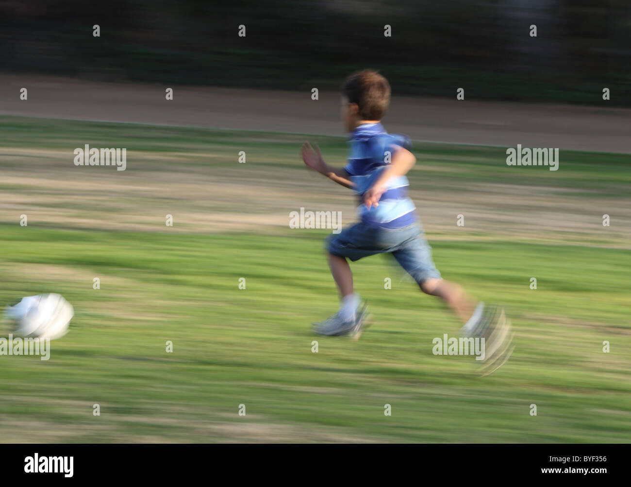 Motion blurred boy running fast after soccer ball on green grassy background Stock Photo