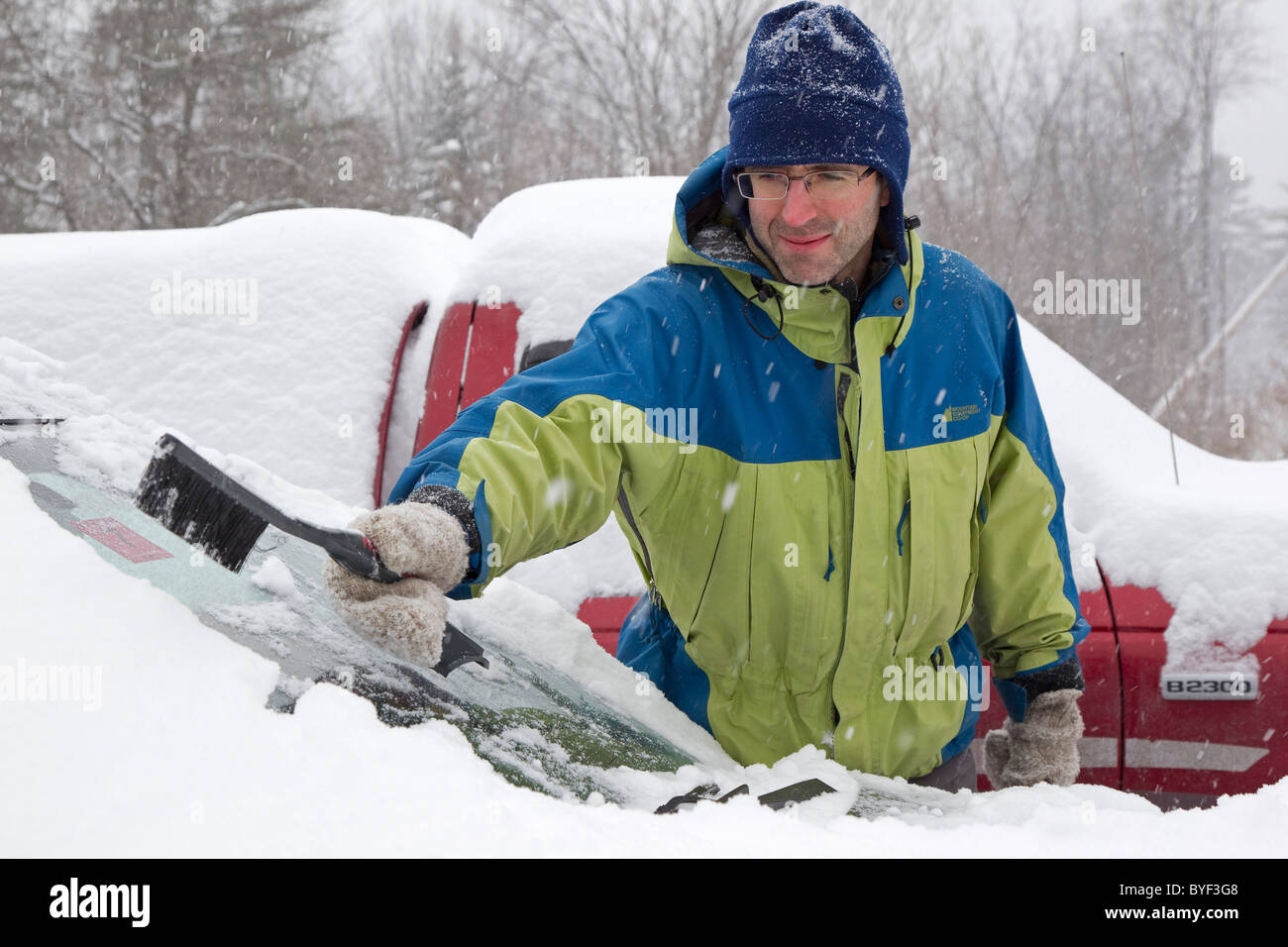 Man scrapes snow from car windshield in winter after heavy snowfall, New England, New Hampshire, USA Stock Photo