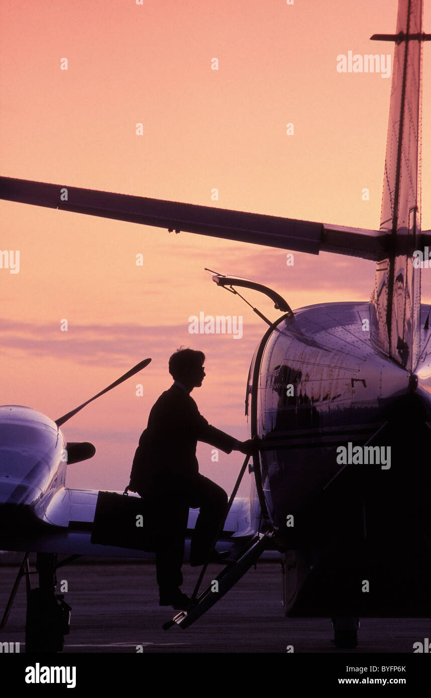 Businessman in silhouette boarding a light aircraft at dawn carrying a ...