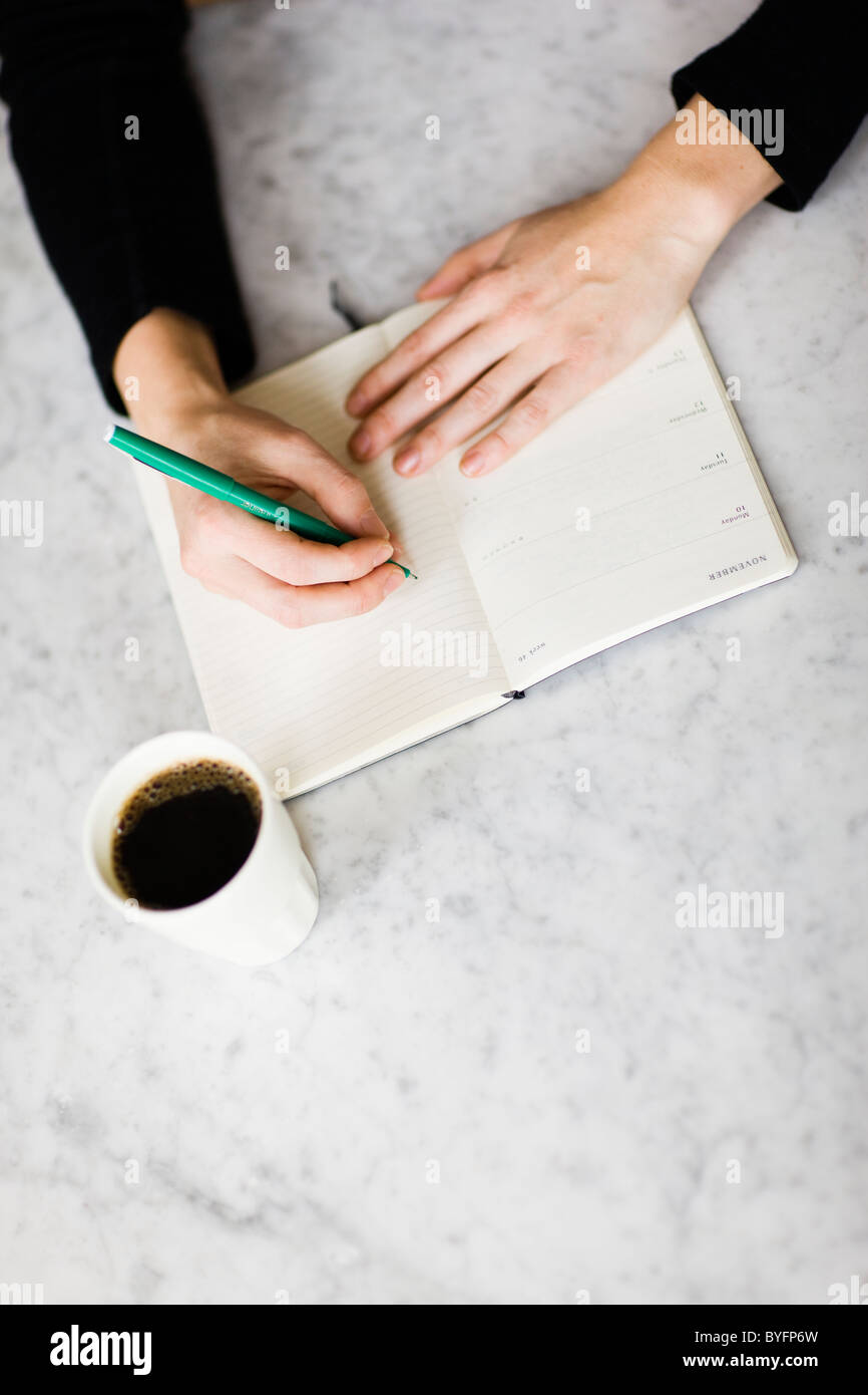Woman writing on diary, coffee on side Stock Photo