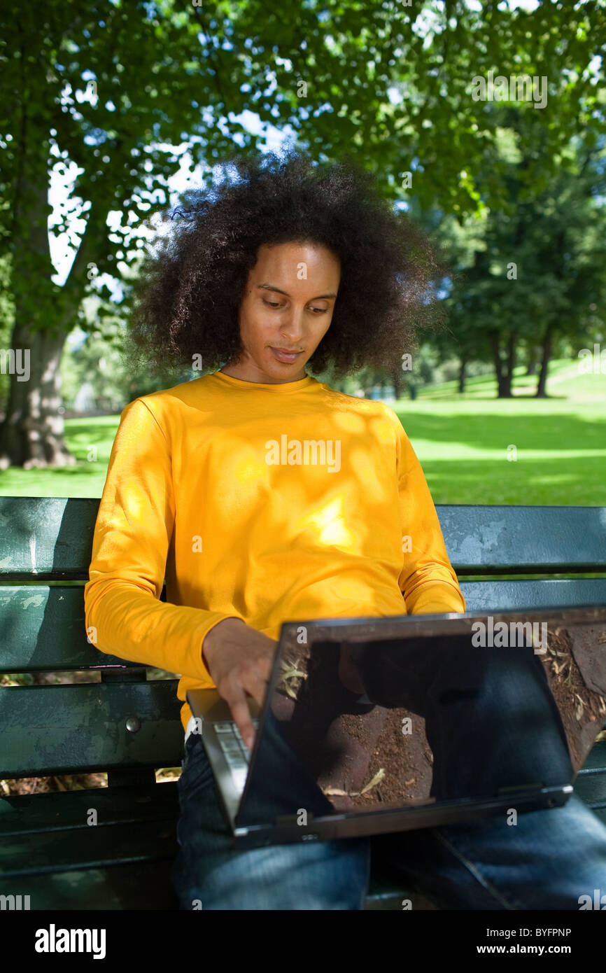 Smiling young man with afro hair sitting on bench with laptop Stock Photo