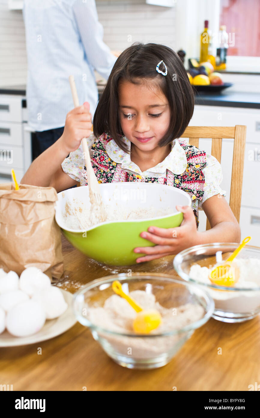 Girl baking in kitchen with mother in background Stock Photo Alamy