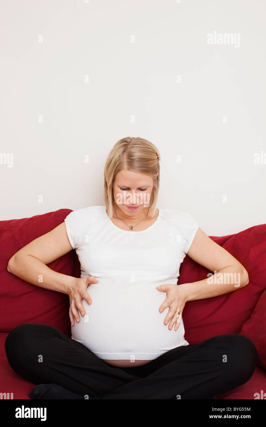Pregnant woman sitting on sofa with hands on belly Stock Photo Alamy