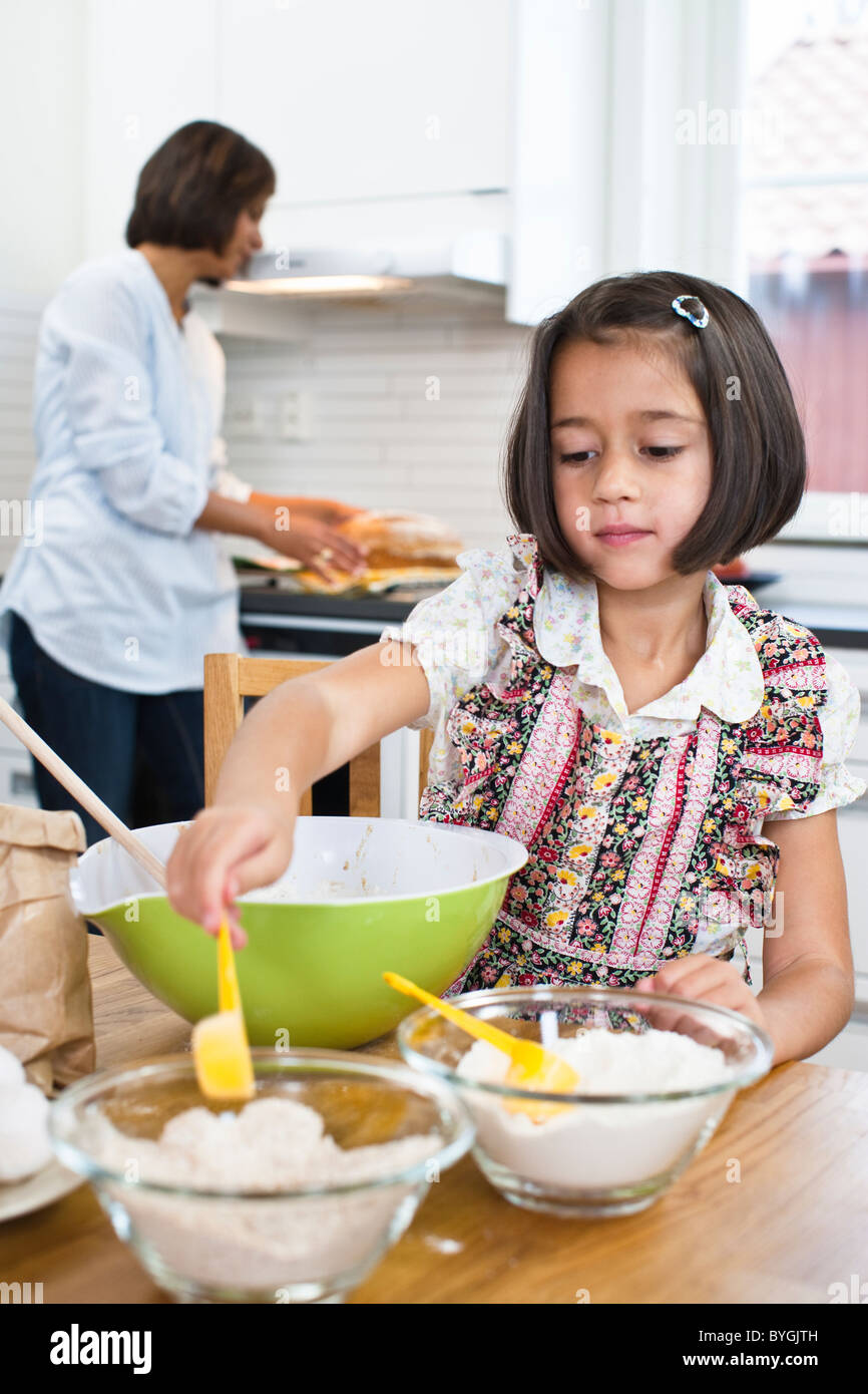 Girl baking in kitchen with mother in background Stock Photo Alamy