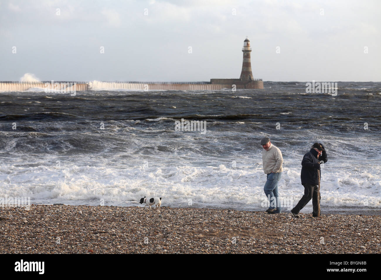 Men walking on Roker beach with a dog in stormy weather, North East England, UK Stock Photo