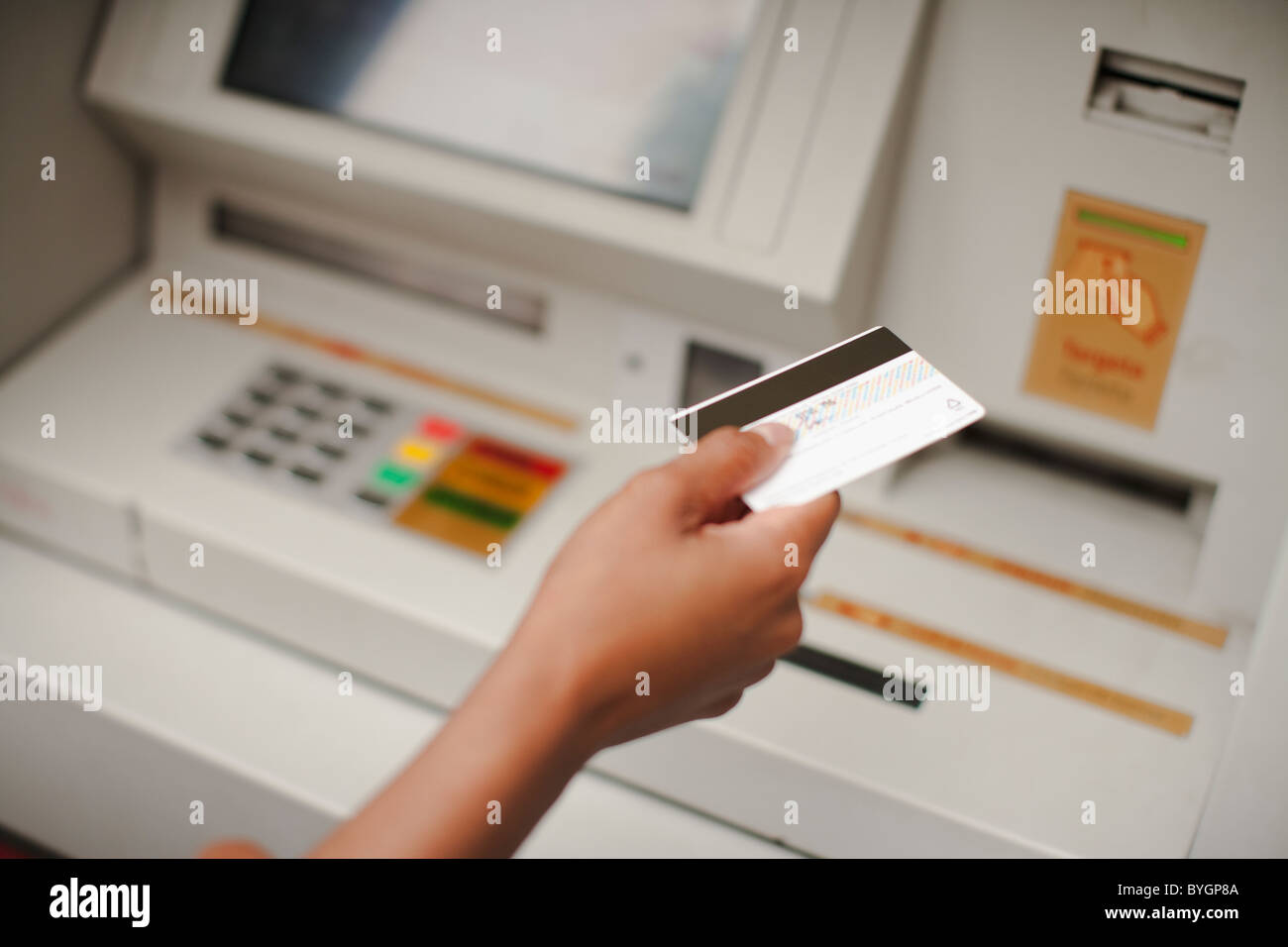 Human hand holding credit card, cash machine in the background Stock Photo