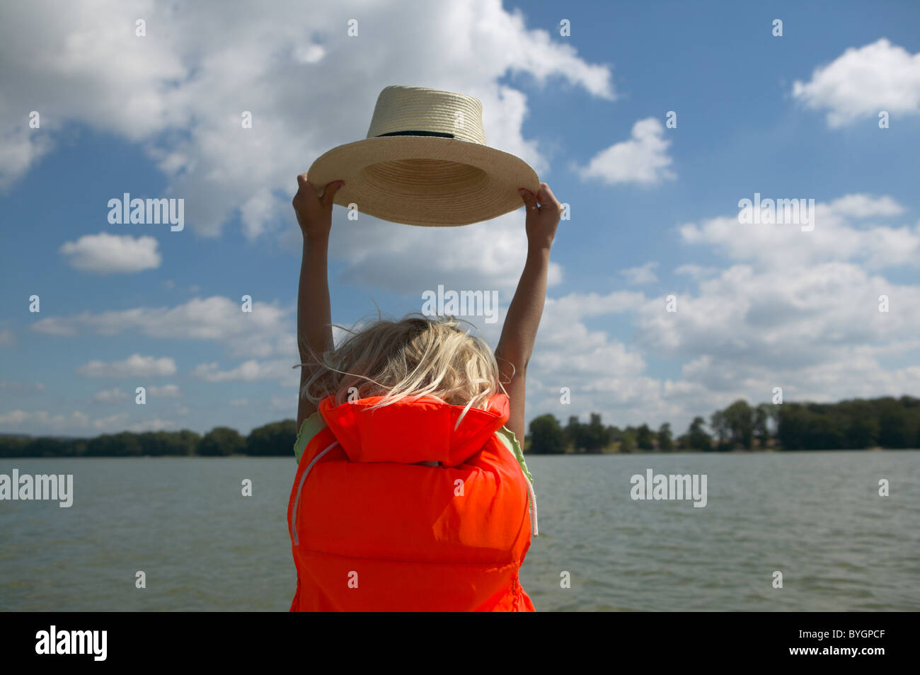 Girl wearing life jacket, holding hat by lake Stock Photo