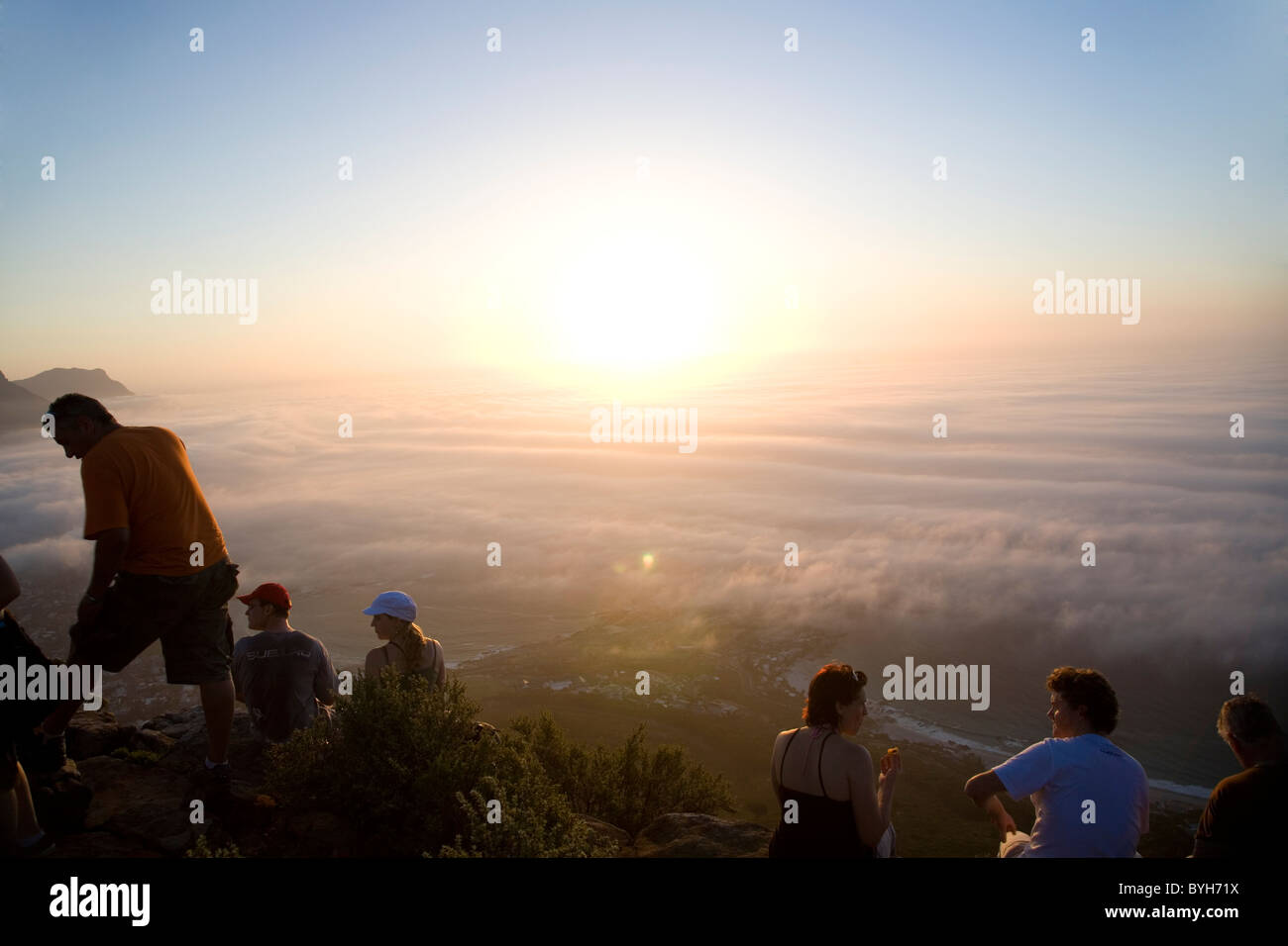 Hikers on top of Lions Head watching sunset above fog - in Cape Town on Summer Solstice 21 December Stock Photo