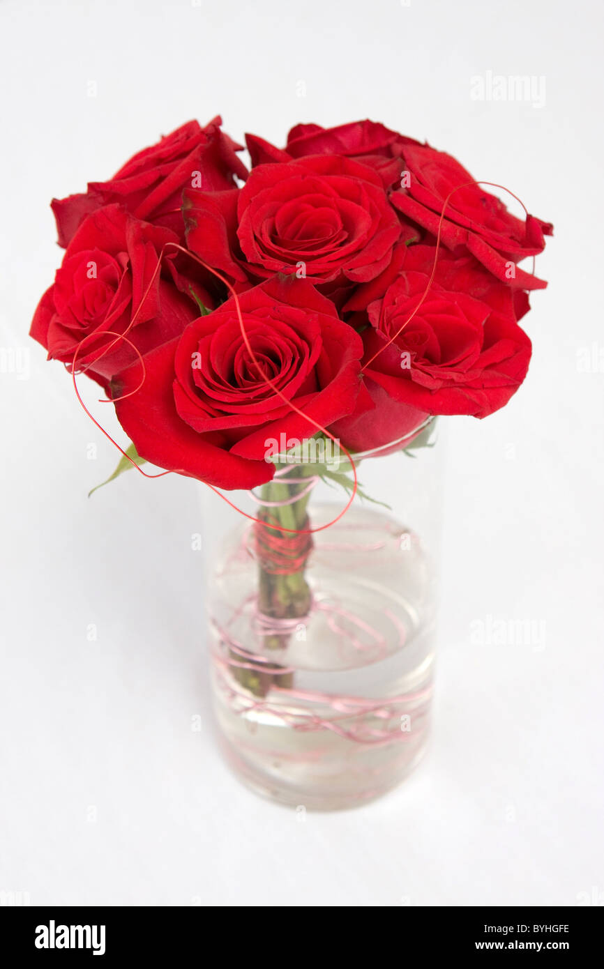 A bundle of red roses sit in water in a clear vase. Stock Photo