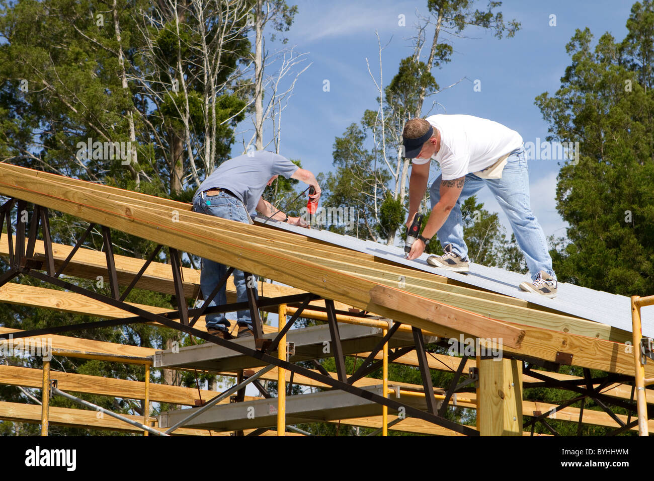 Two roofers use screw-guns to bolt corrugated metal sheets to the roof ...