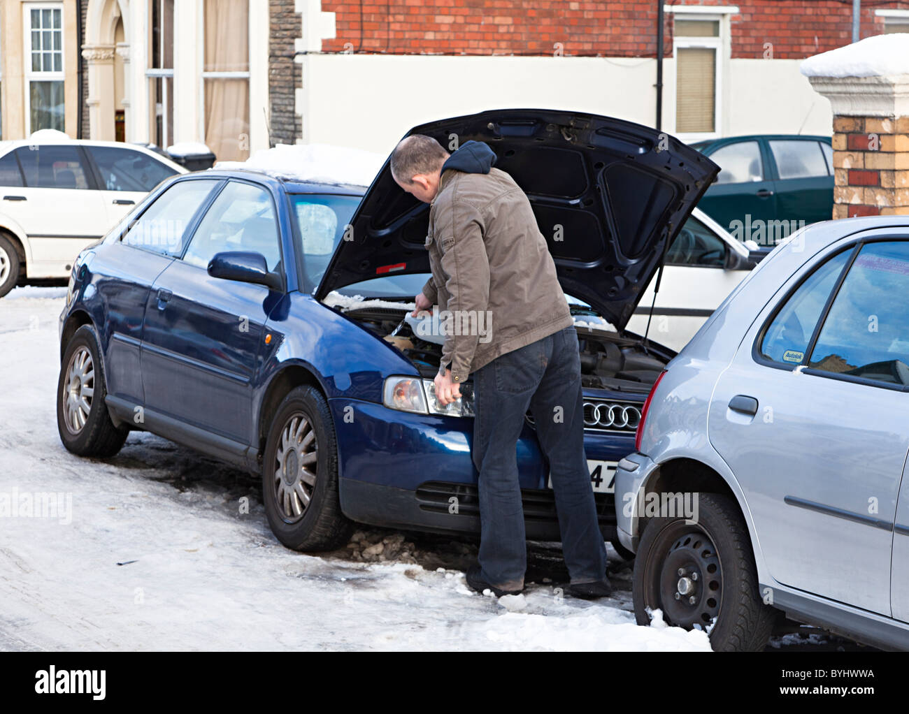 Man in snow in winter filling car with screenwash with deicer Cardiff Wales UK Stock Photo
