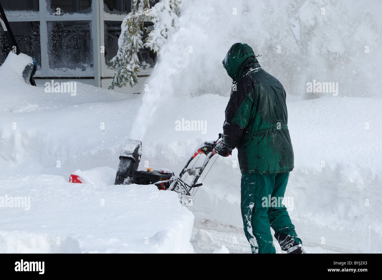 Man using a modern snow blower to clear a driveway the morning after a winter blizzard Stock Photo