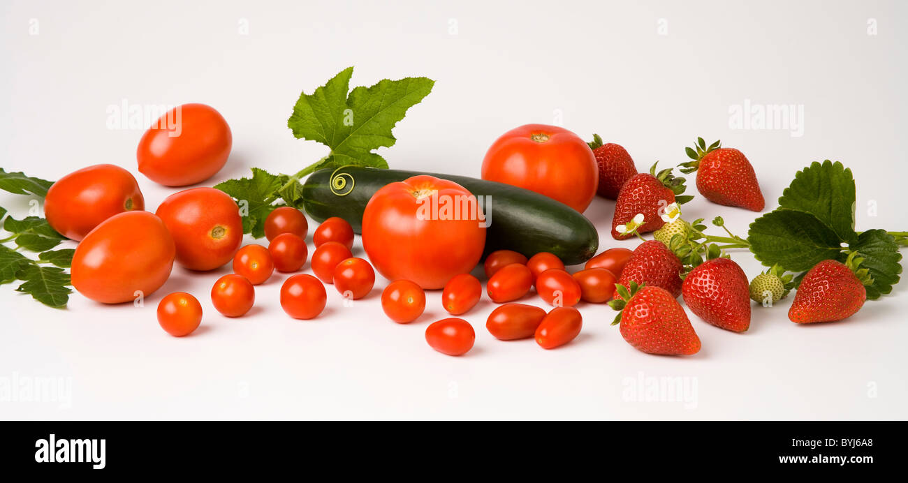 Mixed fresh fruits and vegetables on a white surface; strawberries