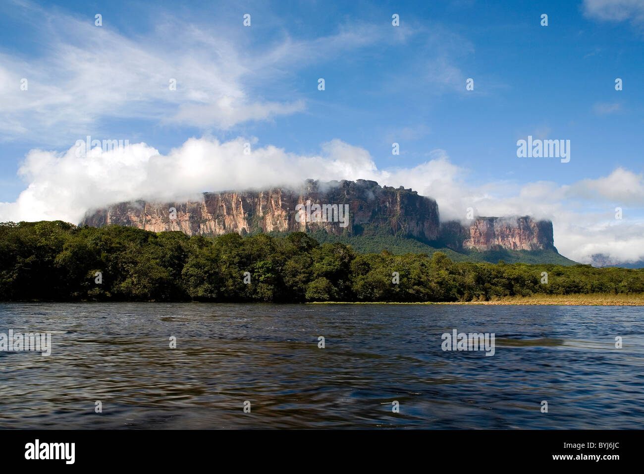 A big Tepui mountain by the coast of a river surrounded by clouds and trees, NATIONAL PARK CANAIMA, GUAYANA, VENEZUELA Stock Photo