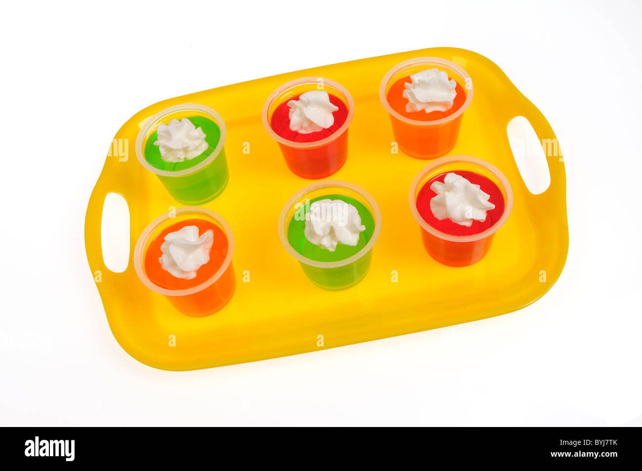 Colorful Jell-o pots with whipped cream topping on yellow tray on white background, cutout. Stock Photo