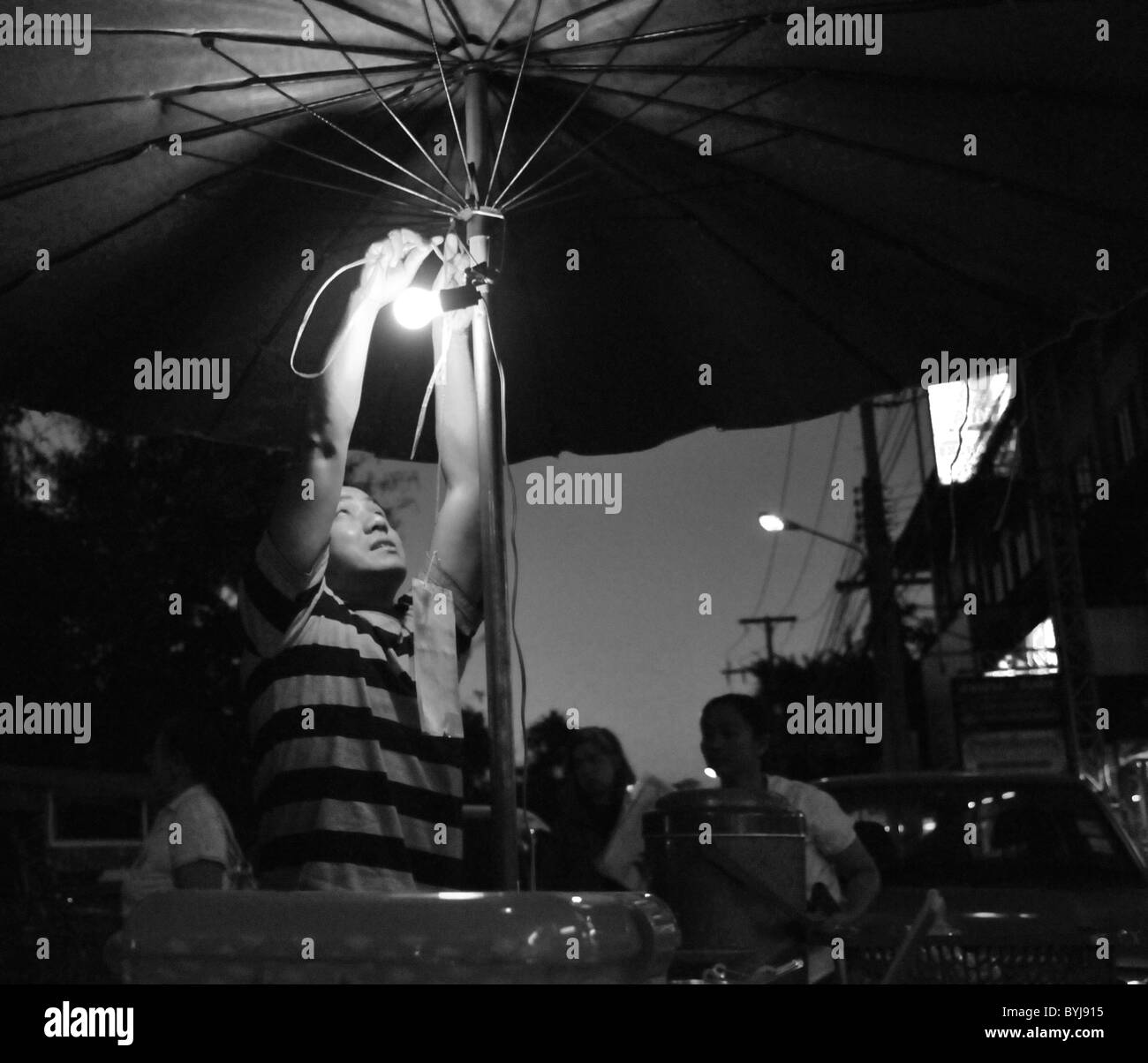 Black and white portrait of a man rigging a light at a Thai night market Stock Photo
