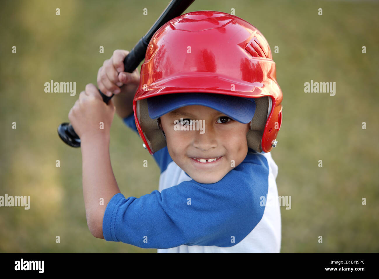 Young Hispanic or Latino boy with red baseball helmet over a blue hat