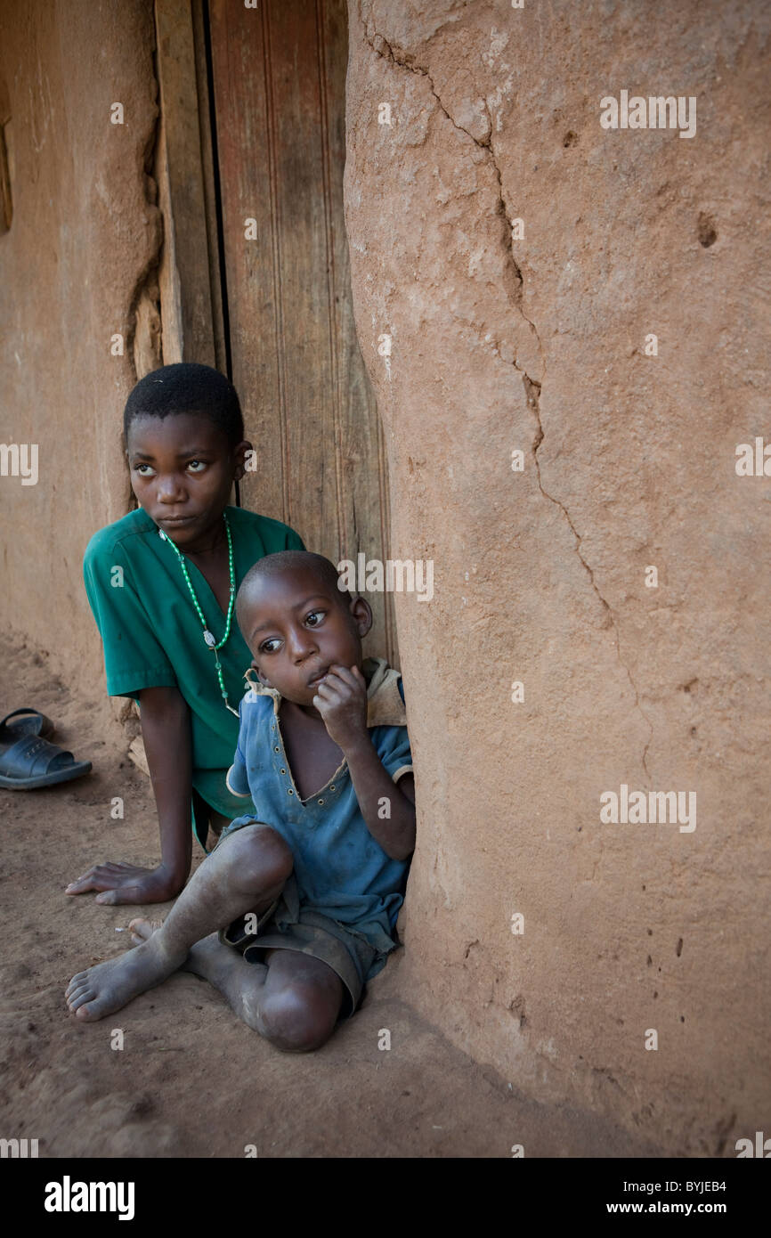 Children sit outside the doorway of their mud house in rural Masaka, Uganda, East Africa. Stock Photo