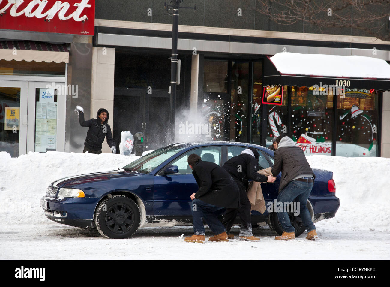 Snowball fight combatants take cover behind car as opponent lobs snowballs. Oak Park Illinois Chicago Blizzard of 2011 Stock Photo