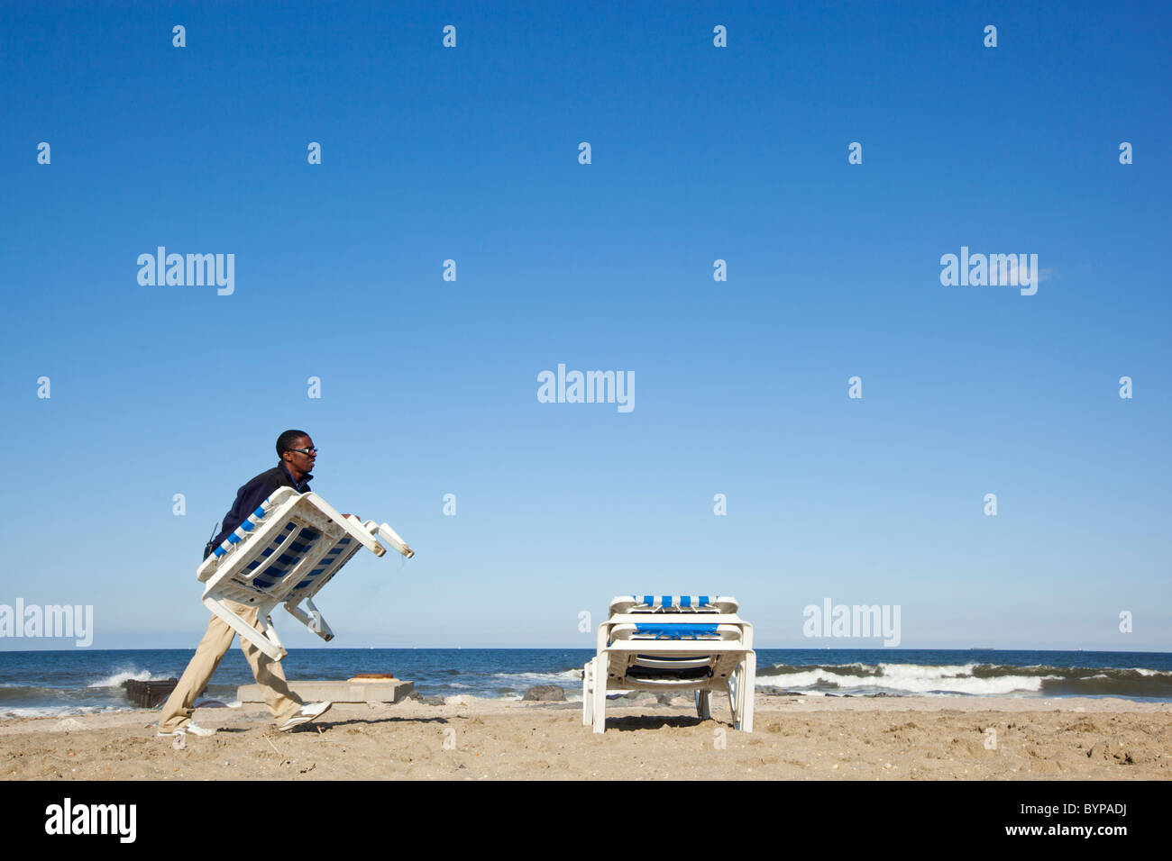 USA, New Jersey, Monmouth Beach, Young man collects resort beach chairs on empty beach on cool early summer afternoon Stock Photo