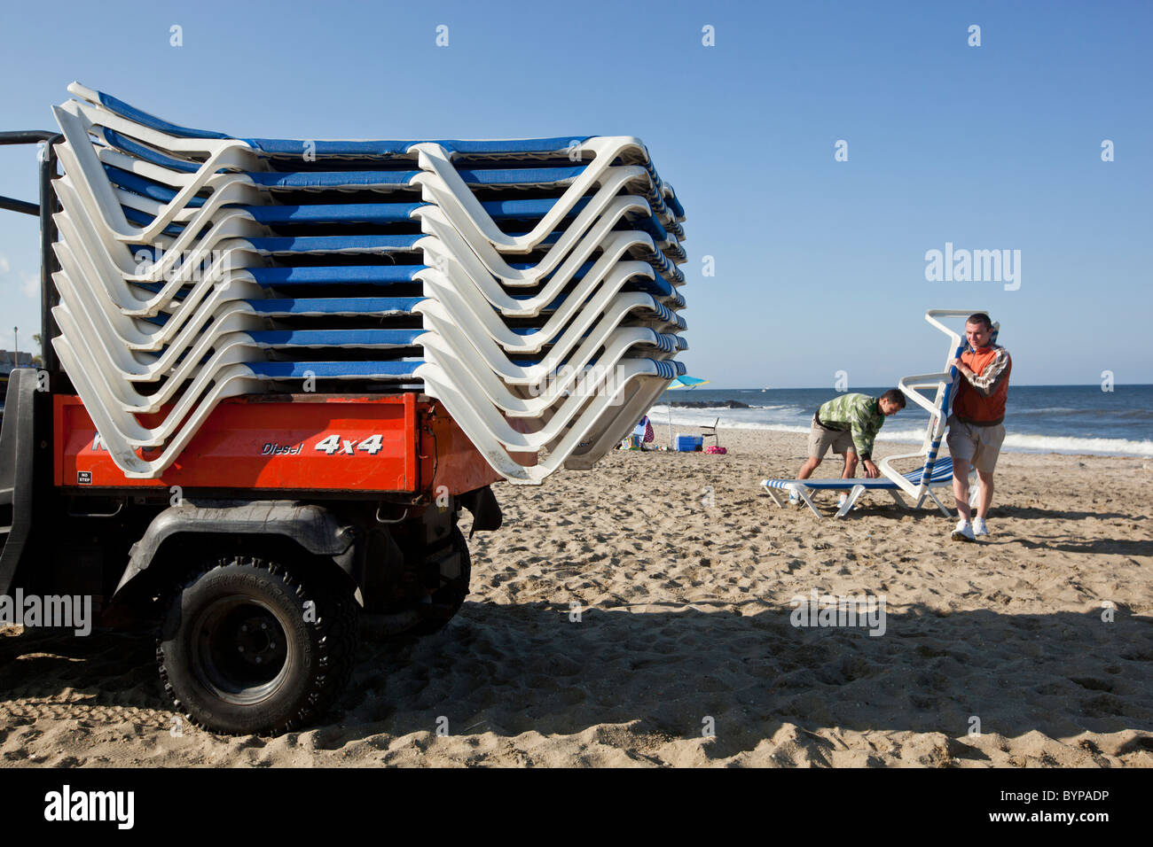 USA, New Jersey, Monmouth Beach, Young men collect resort beach chairs on empty beach on cool early summer afternoon Stock Photo