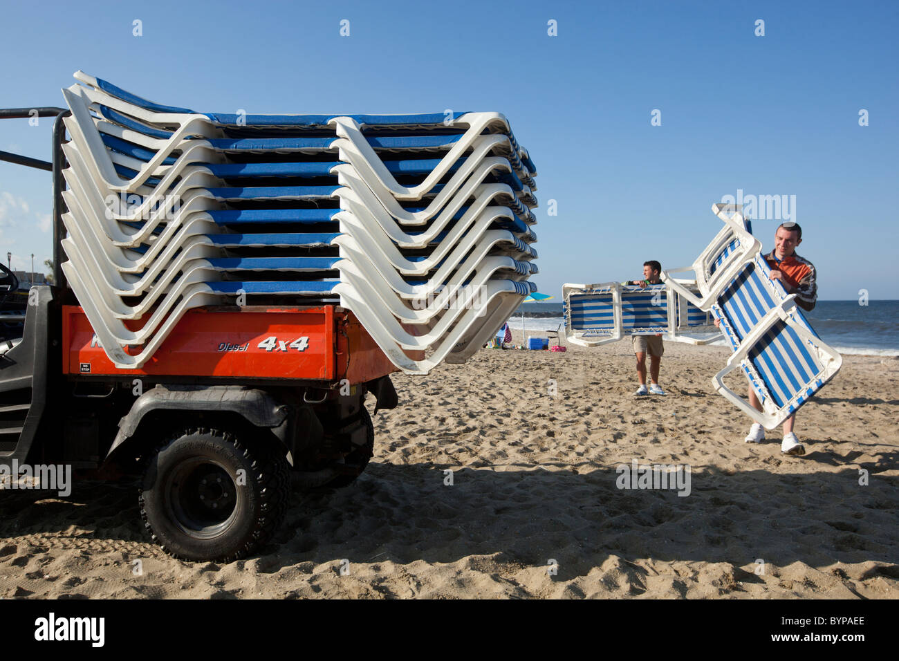 USA, New Jersey, Monmouth Beach, Young men collect resort beach chairs on empty beach on cool early summer afternoon Stock Photo