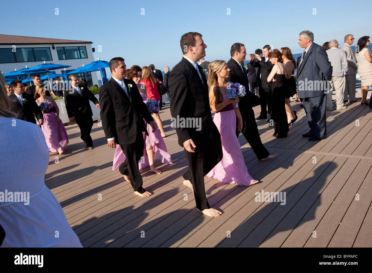 USA, New Jersey, Monmouth Beach, Members of wedding party walk barefoot down boardwalk during beach wedding on summer afternoon Stock Photo