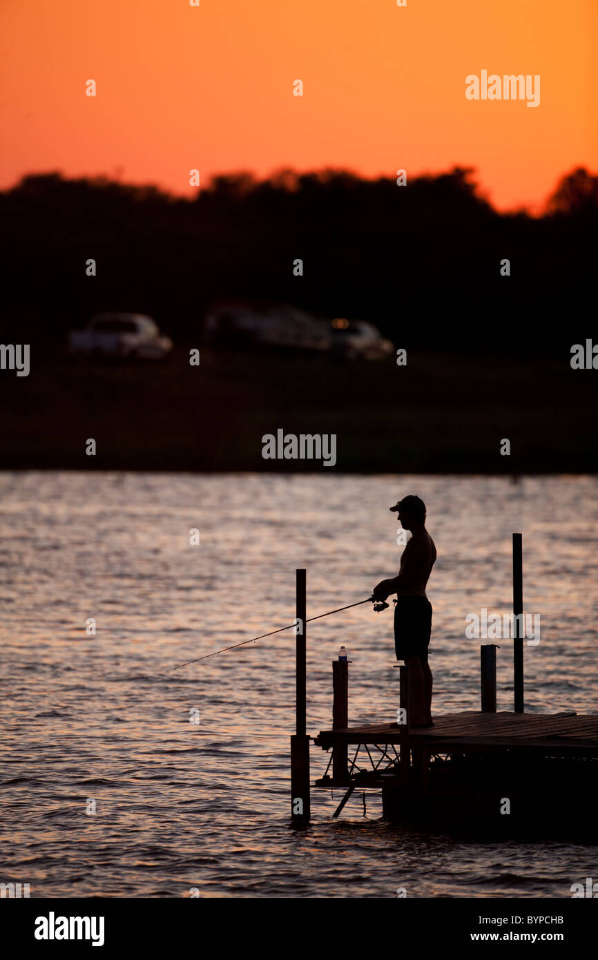 USA, Texas, Lake Arrowhead State Park, Young man hold fishing rod while fishing from freshwater dock at sunset on summer evening Stock Photo