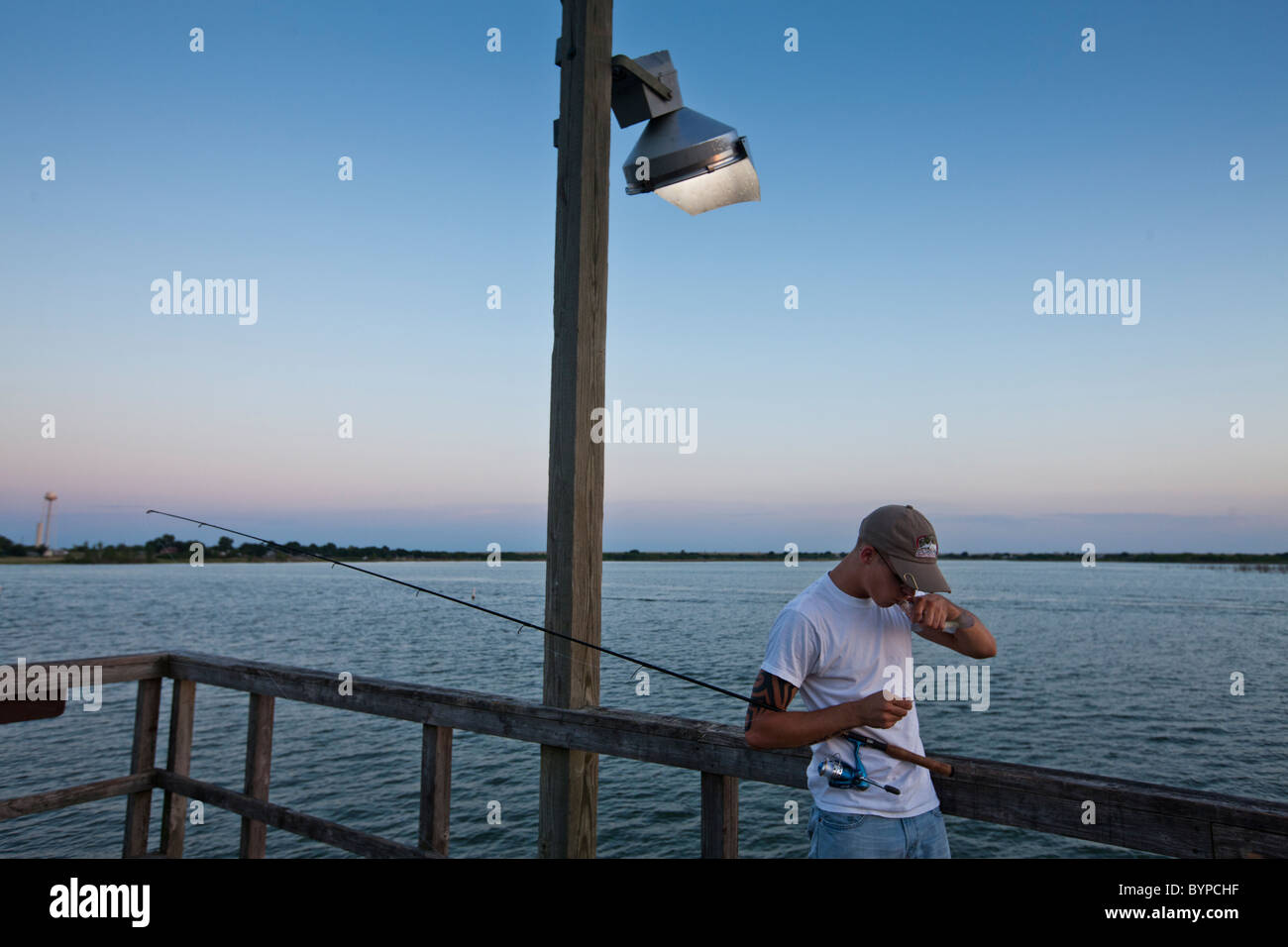 USA, Texas, Lake Arrowroot State Park, Young man kisses fish for good luck while fishing from public dock on summer evening Stock Photo