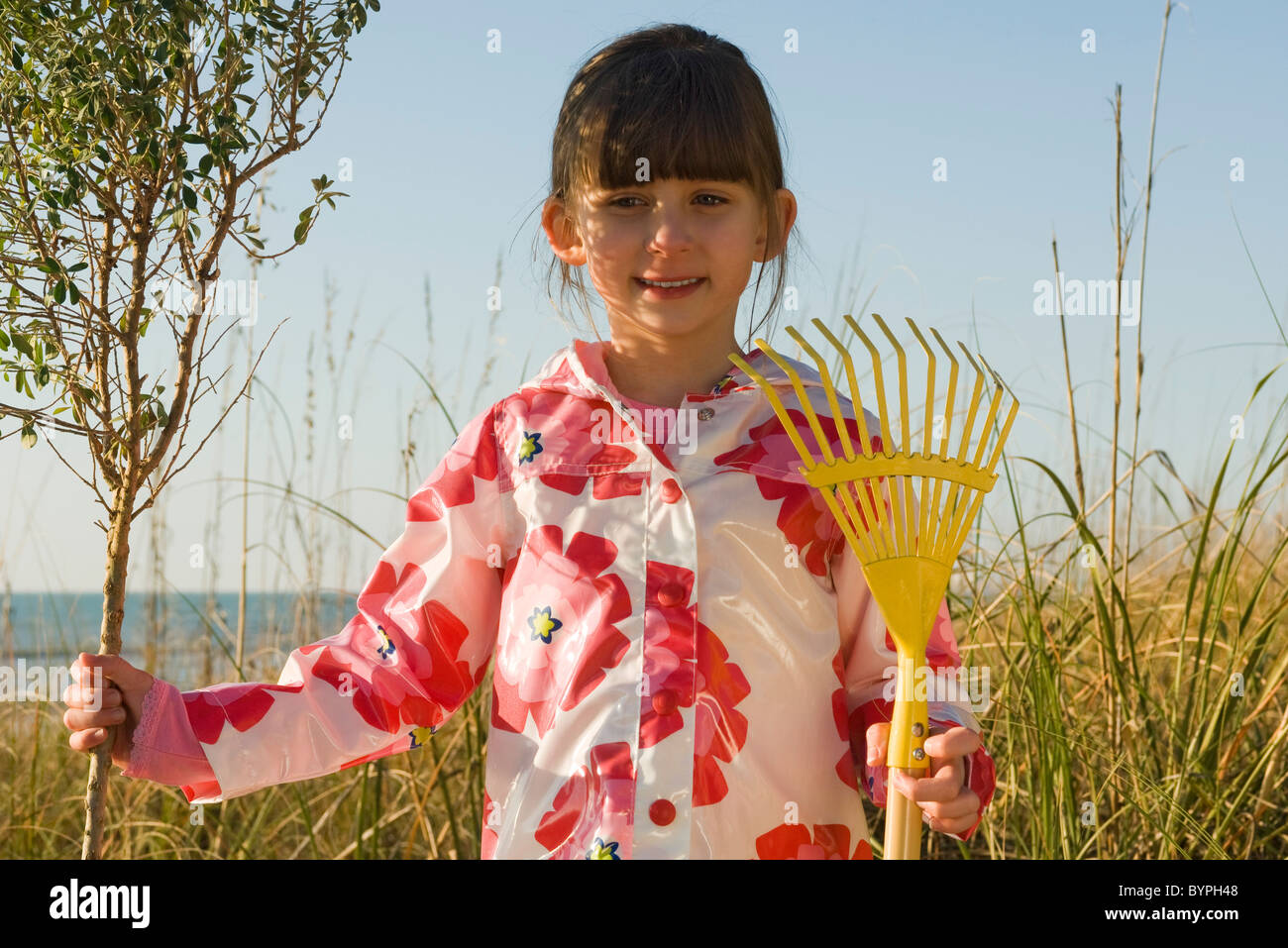 Young girl with gardening rake standing next to tree sapling Stock Photo