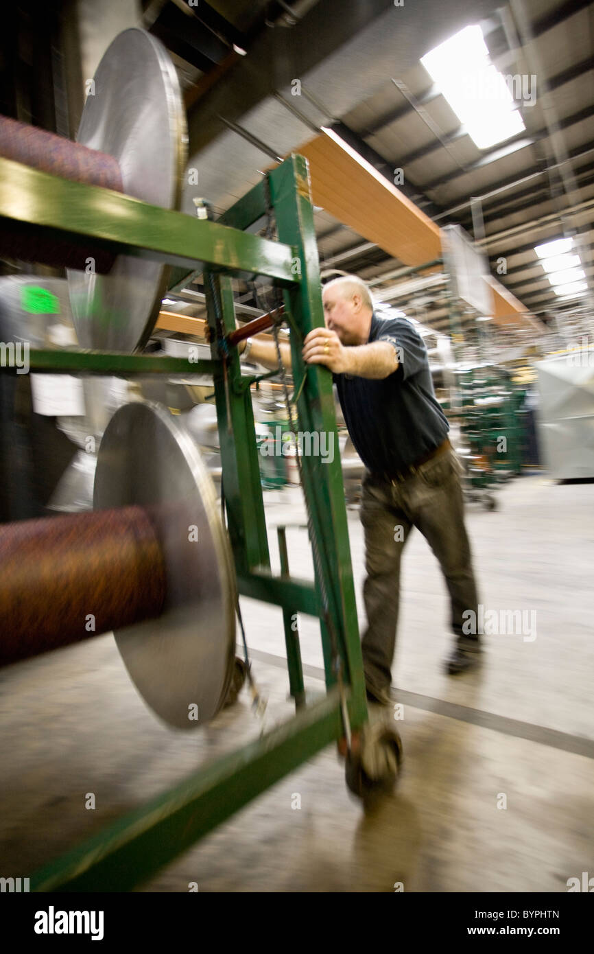 Textile worker setting up warp beams on weaving machine in carpet tile factory Stock Photo