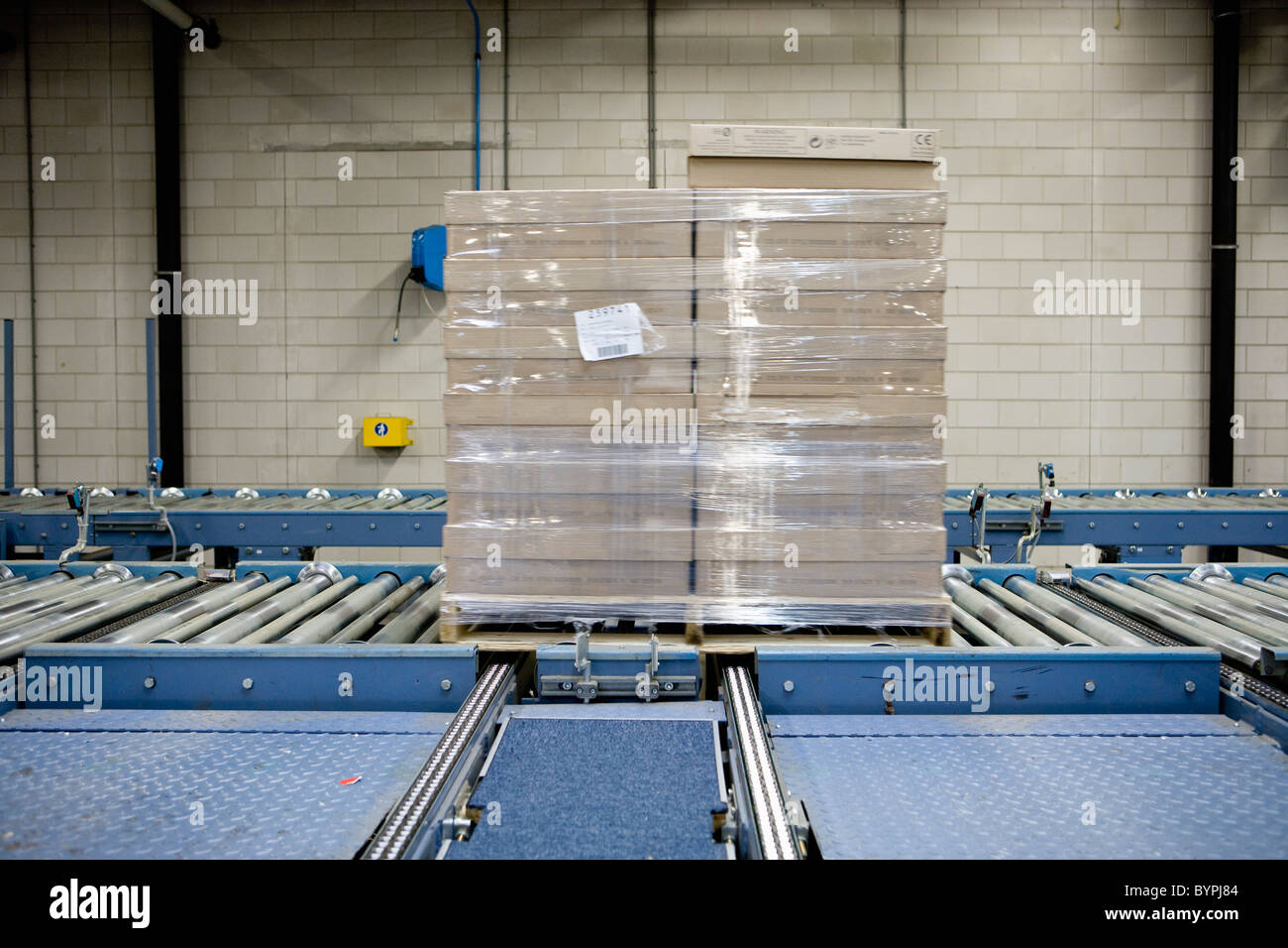Wrapped pallet of cardboard boxes on conveyor belt in carpet tile