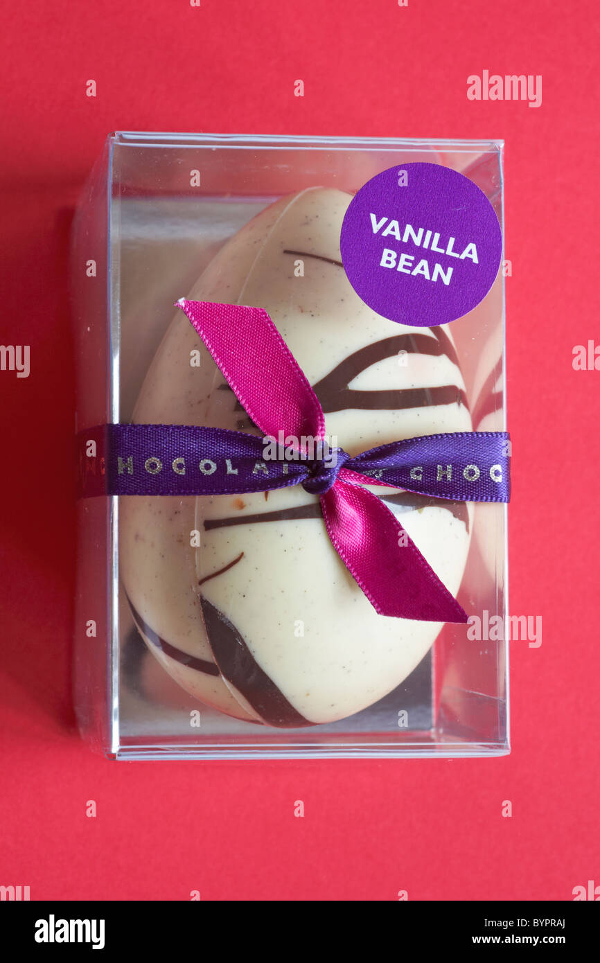 Vanilla bean white chocolate Easter egg in plastic casing set against red background Stock Photo