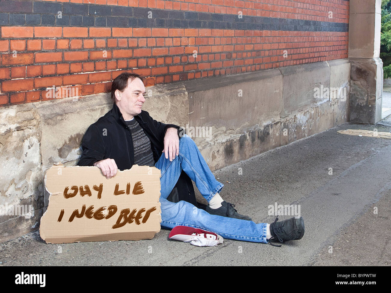 adult male sat begging with a cap and a cardboard sign with "why lie I