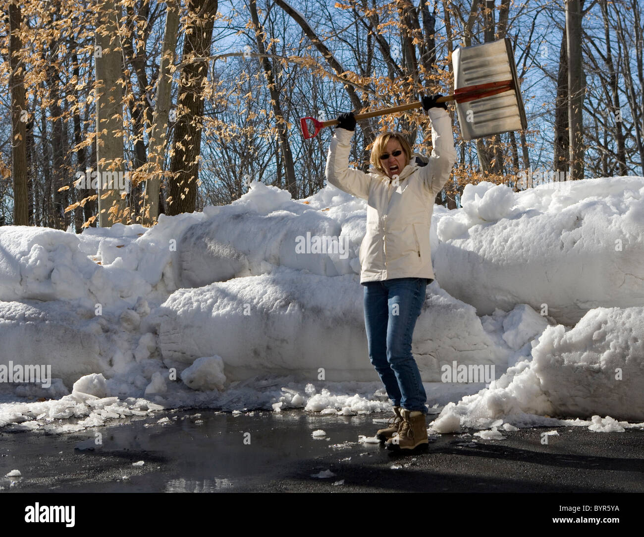 Woman with snow shovel over head in defiance of winter Stock Photo