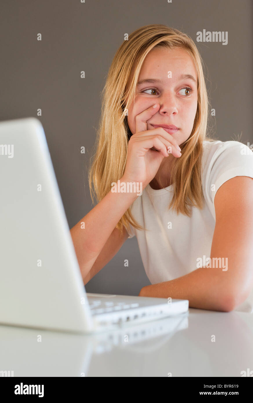 a girl in white and using a white laptop computer with a look of contemplation; benalamadena costa, malaga, andalusia, spain Stock Photo