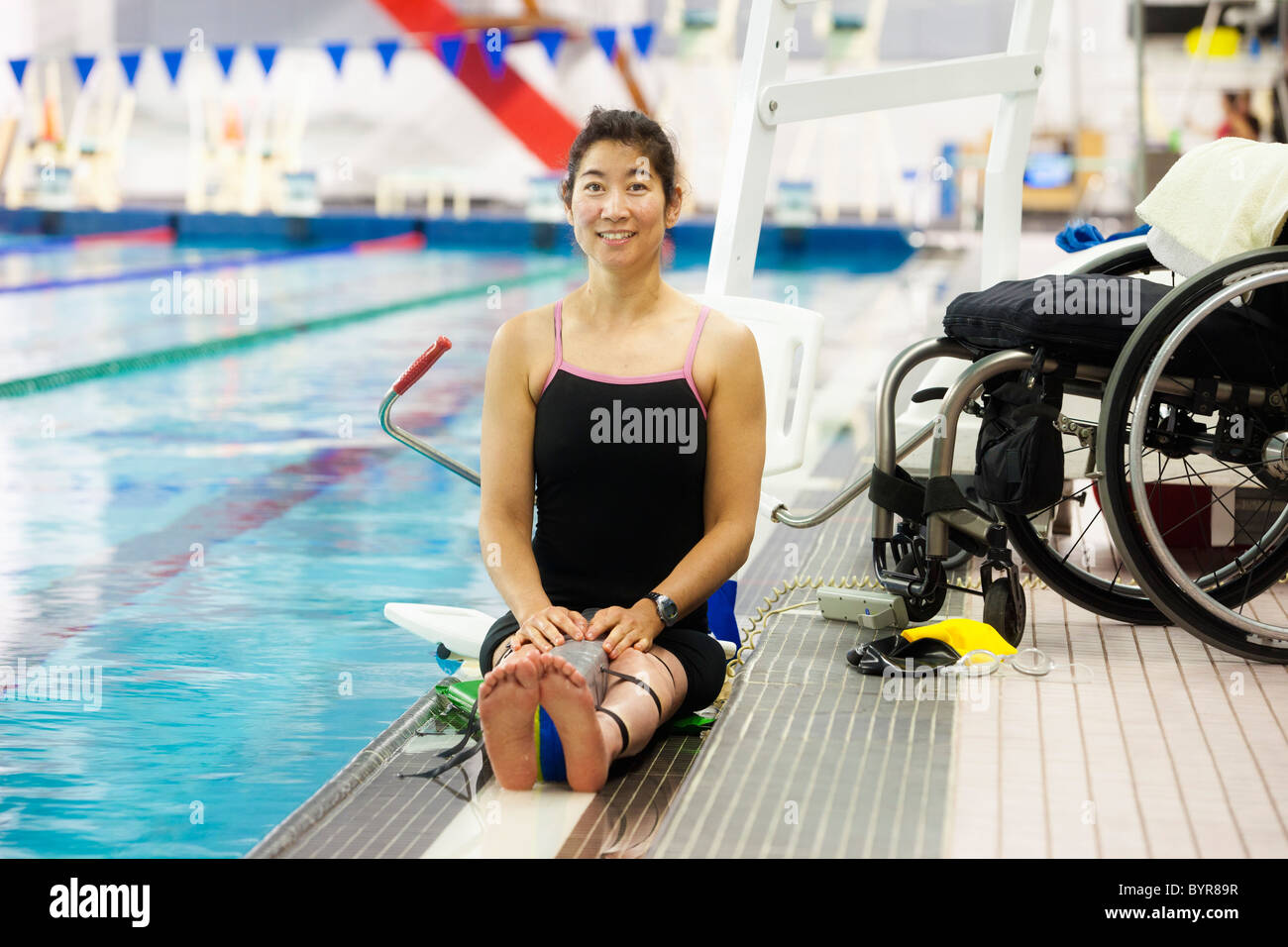 a paraplegic woman sits at the edge of a swimming pool on a lift near a