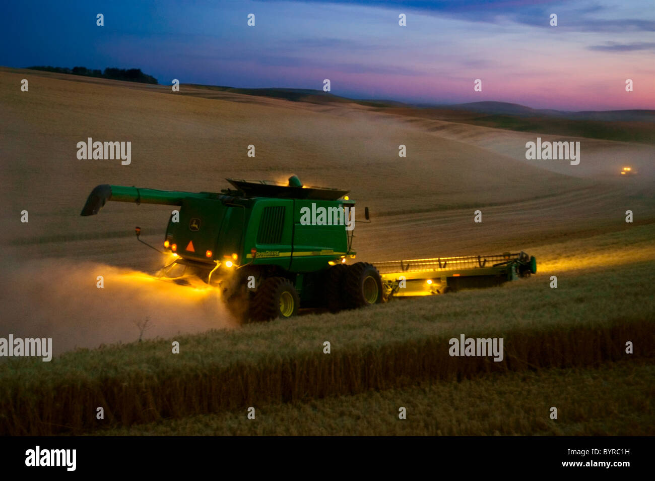 Agriculture - A John Deere combine harvests wheat at dusk in the Palouse region / near Pullman, Washington, USA. Stock Photo