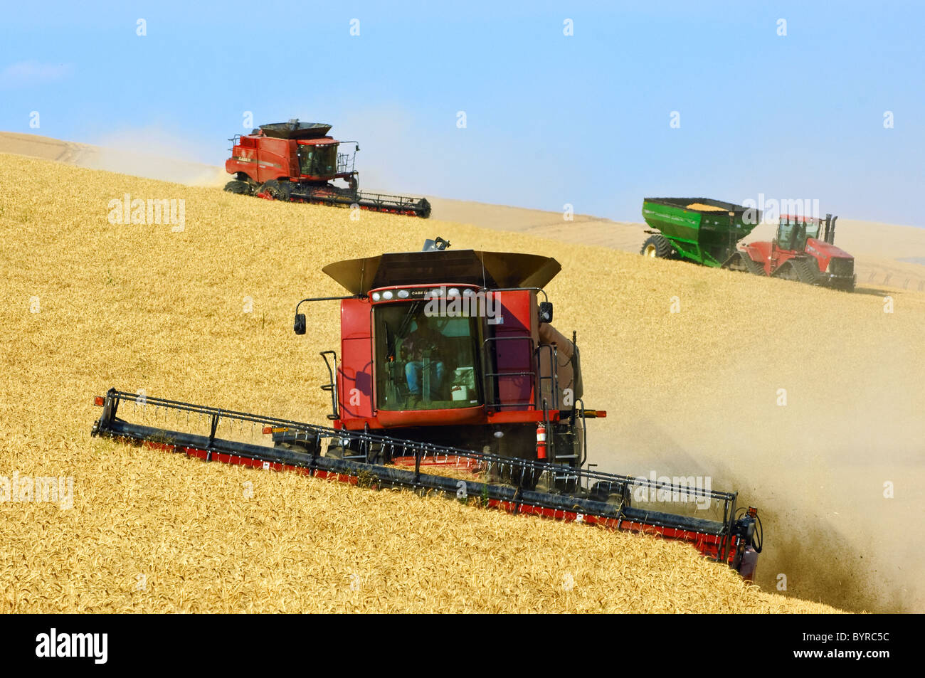 Two Case IH combines and a grain cart pulled by a tracked tractor harvest wheat on the steep hillsides of the Palouse Region. Stock Photo