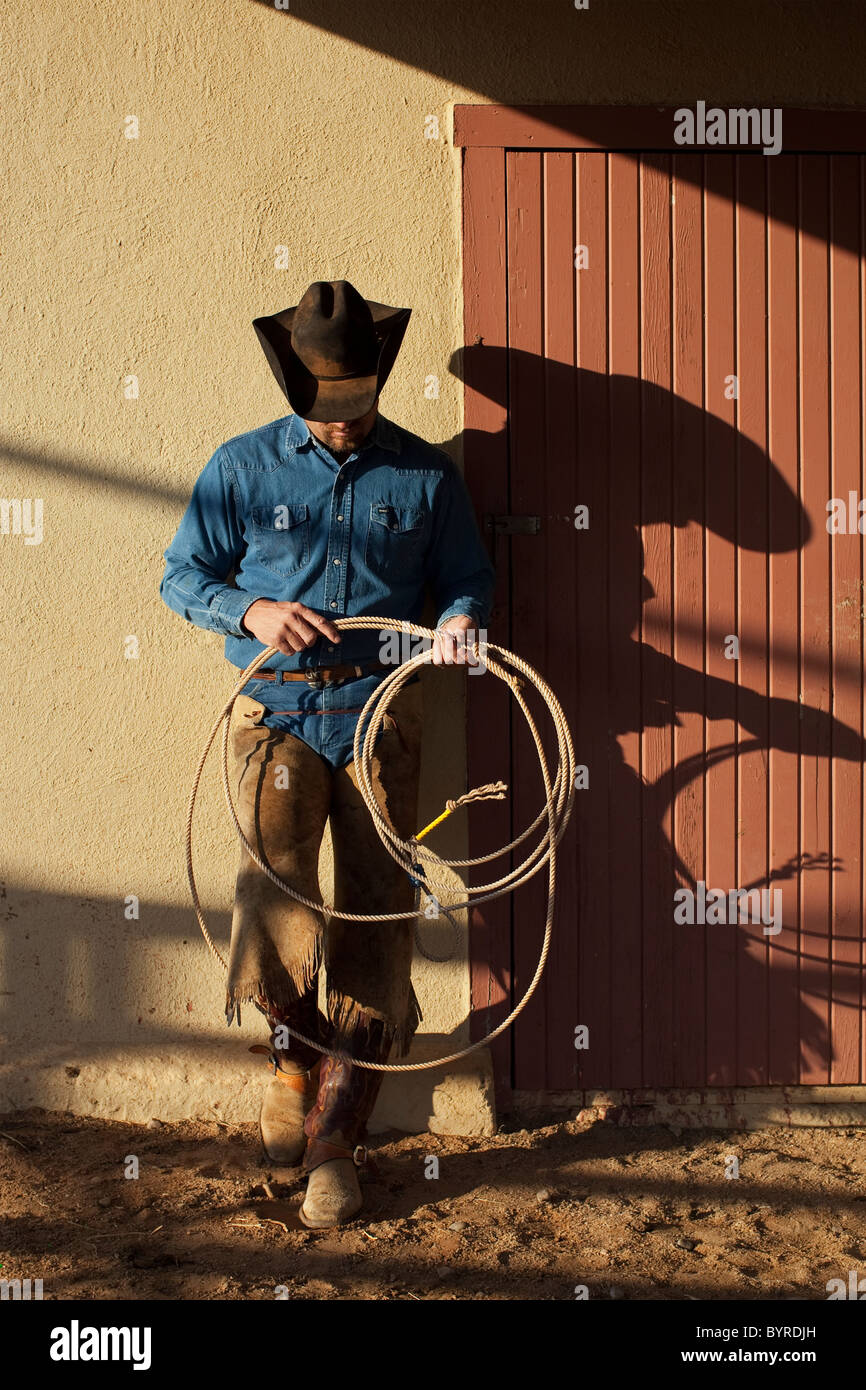 Agriculture - Cowboy with a lasso rope standing against a barn in evening light / Childress, Texas, USA. Stock Photo