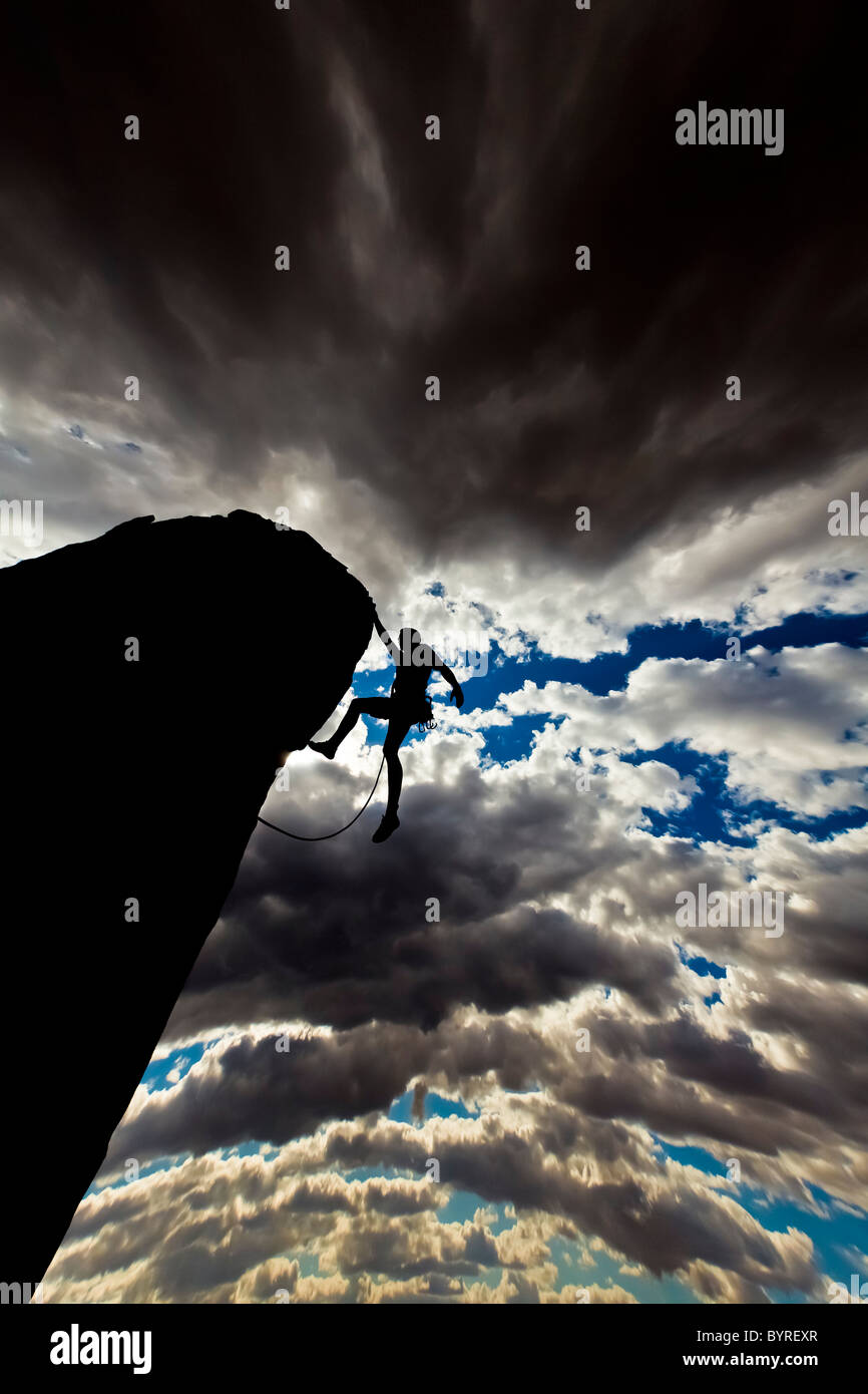 Rock climber struggles for his next grip on the edge of an overhanging spire. Stock Photo