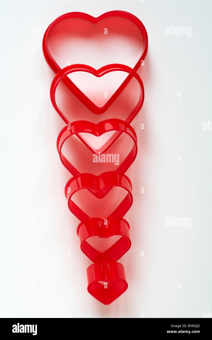 Line of red heart shaped Valentine cutters decreasing in size set against white background - concept falling out of love Stock Photo