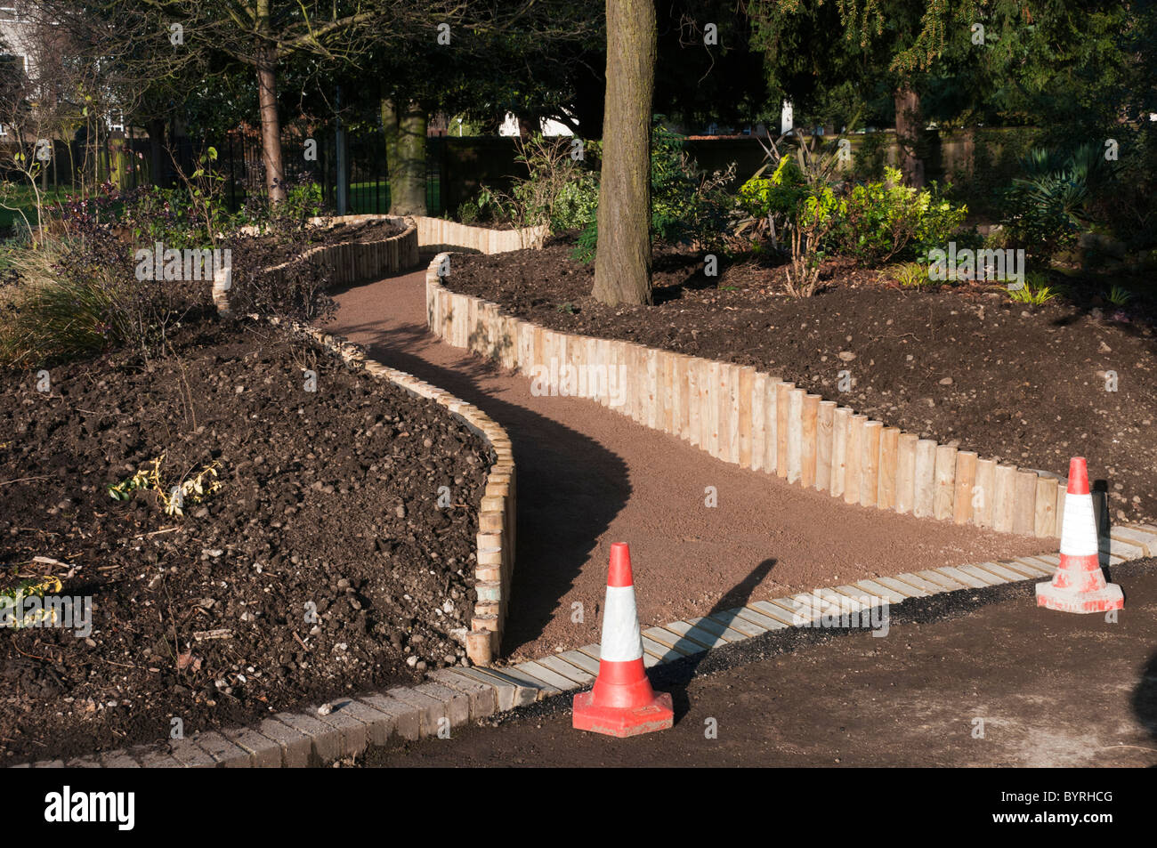 A new, edged, curving path made through an existing raised bed flowerbed in a public park. Stock Photo