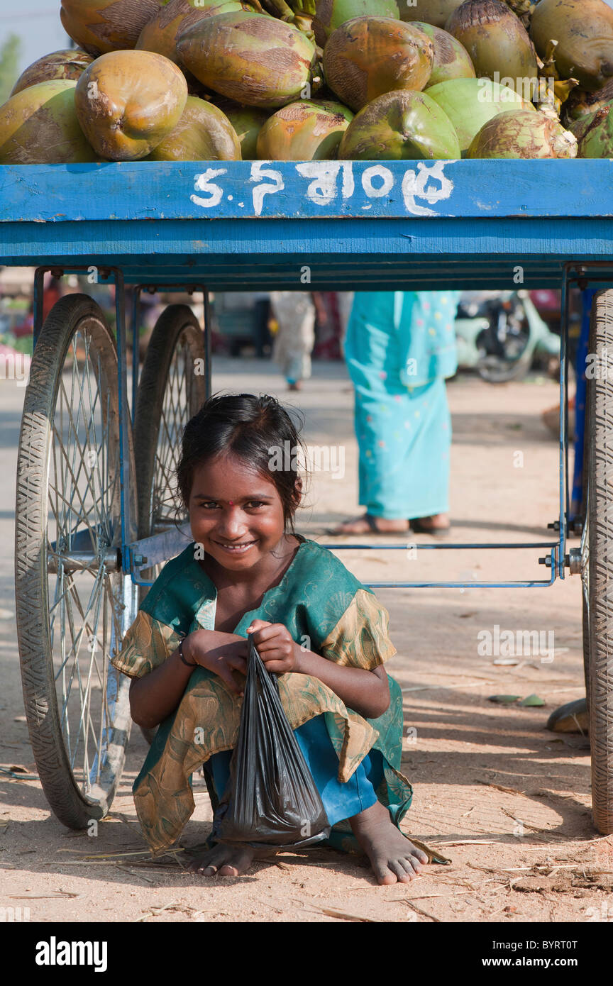 Happy young poor lower caste Indian street girl smiling sitting under a coconut stall. Andhra Pradesh, India Stock Photo