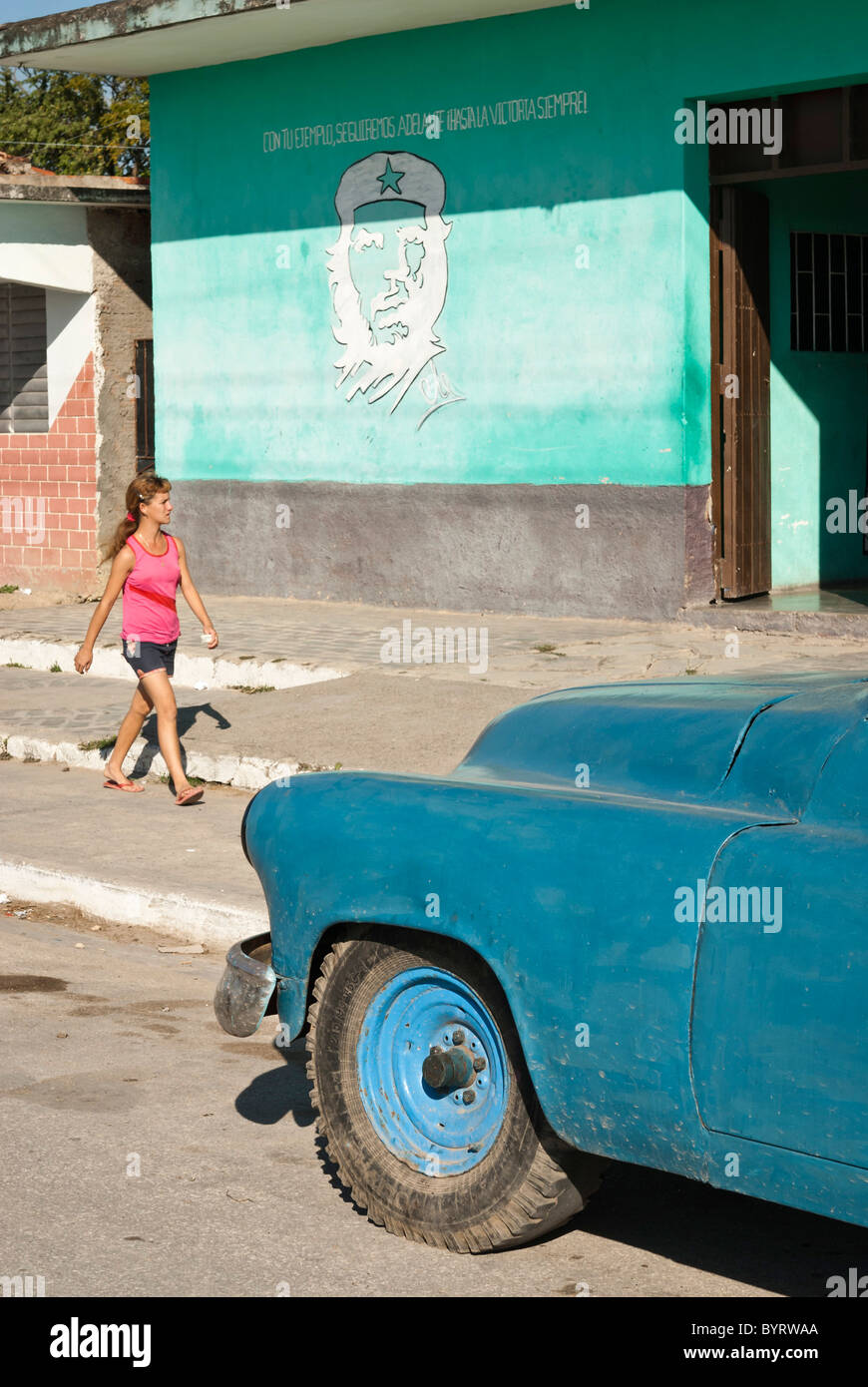 Old car on the street and a woman walking by a painting of Che Guevara, Sancti Spiritus, Cuba Stock Photo