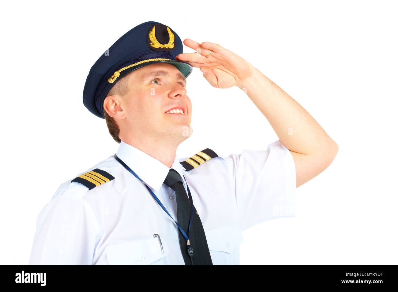 Cheerful airline pilot wearing uniform with epaulets and hat looking upwards, standing isolated on white background. Stock Photo