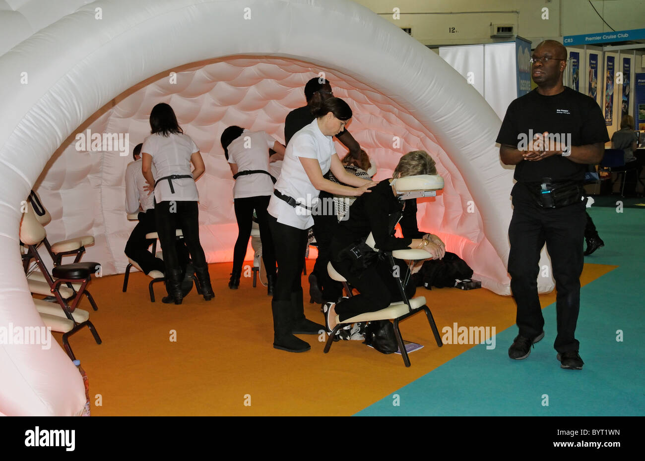 Massage therapists working from a padded cell like exhibition stand massaging visitors to a travel show in Earls Court London UK Stock Photo