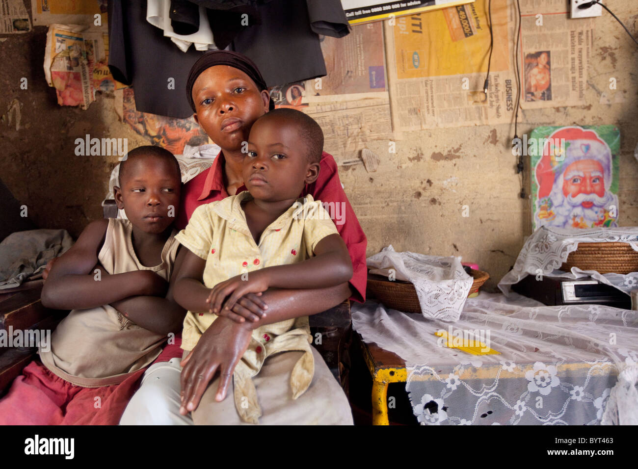 An HIV positive single mother sits in her living room with her two daughters in Kampala, Uganda, East Africa. Stock Photo
